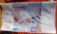 Front view of Munchkin baby change pad in original packaging, showing product name, image of baby, and description.