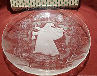 Large oval pressed glass Christmas platter with frosted St. Nicholas carrying a sack and surrounded by a village scene. Original green and white box visible.