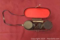 Top view of black leather case with red interior, containing black Sears binoculars with lens covers inside.