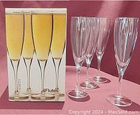 Four clear champagne flutes displayed next to original box showing branding and image of glasses.
