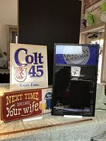 Three beer signs included in the lot: a white illuminated Colt 45 sign, an electric Guinness Black Lager sign, and a wooden Pabst Blue Ribbon humorous sign.