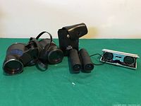 Three pairs of binoculars arranged on a green surface with one Nikon carrying case.