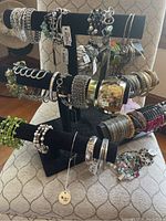 Multiple bracelets displayed on black bracelet racks showing a variety of styles, beads, rhinestones, and metal bangles separated in three tiers.