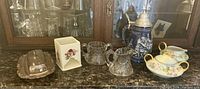 Photo of the entire lot showing the butter dish with cover, square floral container, clear glass creamer and sugar bowl, ceramic beer stein, and ceramic floral creamer and sugar set