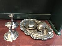 Group photo of two candle sticks, ornate tray, covered butter dish, and pig figurine on wood floor.