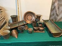 Photo showing full lot of copper and metal items including decorative plate, vases, trays, and containers on green cloth surface.