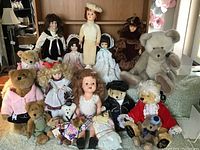 Full lot of vintage dolls, teddy bears including Boyds bears, and plush dolls arranged in rows on a chair and nearby furniture.