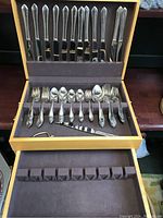 Photo of entire flatware set arranged inside wooden case showing knives, forks, spoons and serving knife.