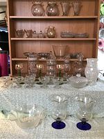 Full shot of the entire glassware collection including shelves withware, multiple diverse glass items arranged on a white cloth surface.