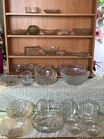 Glass serving ware including textured clear glass bowls and dishes of various sizes and patterns displayed on a shelf and table.