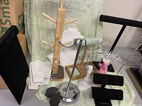 Various jewelry display stands including black velvet padded displays, wooden necklace holder, metal bracelet holder, and white padded tray.