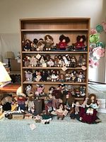 Wooden shelving unit filled with multiple cloth rag dolls arranged across four levels and on the tabletop