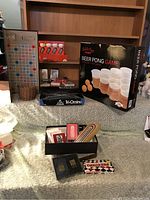 Photo showing Scrabble board, Beer Pong Game, golf balls, Tri-Ominc box, and other game boxes on a couch