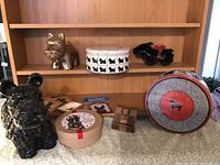 Photo showing large black Scottie figurine, gold Scottie figurine on shelf, two Scottie tins, and black Scottie bowl with smaller bowl inside on table surface.