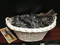 Photo showing a large pile of mixed silverware including forks, knives, and spoons resting inside a white woven basket with a product pamphlet on the side. Basket not included.