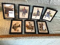 Seven framed soldier pictures arranged in two rows on carpeted surface with measuring ruler for scale