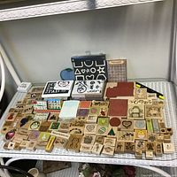 Photo of a large assortment of wooden mounted rubber stamps with various designs arranged on a shelf with two storage boxes and an ink pad visible.
