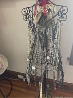 Photo showing a variety of costume necklaces displayed on a decorative wire mannequin with beads in colors such as white, cream, black, and green.