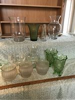 Nine decorative glass vases arranged on carpet; includes clear, frosted orange, green ribbed, and other styles.
