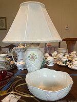 Photo showing the Belleek Georgian shell bowl in white ceramic with embossed shell design, pink shading, and gold rim alongside the floral pattern lamp with white shade.