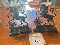 Pair of vintage brass unicorn bookends on wooden table, showing a dark brass patina with detailed unicorn figures.