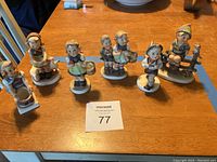 Lot of six vintage Hummel figurines arranged on a wooden table showing various child characters in traditional clothing.