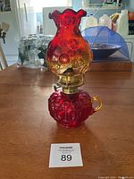 Full view of Indiana Glass hurricane lamp showing red base with ornate patterns, brass wick holder, and red to amber ombre glass chimney with scalloped edge.