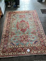 Full view of the rectangular Kazak carpet lying on floor, showing overall pattern and color palette in reds, pastels, and blues.