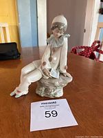 Front view of Lladro porcelain Pierrot clown figurine sitting and reading a letter on naturalistic base.