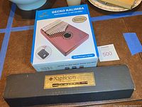 Photo showing boxed Gecko professional 17 key solid mahogany kalimba alongside black hard case for Xaphoon pocket sax.