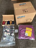 Overview of sealed JUKI box, tote in plastic, box of thread cones and bag of thread cones on floor