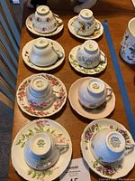 Top-down view of all 8 teacups upside down on matching saucers showing patterns and brands on bottom