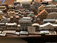 Wide array of wooden historical building models arranged in rows on a table, showing multiple architectural styles and detailed facades.