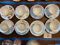 Top down view of all 8 vintage fine china teacups and matching saucers arranged in two rows showing various floral designs and patterns