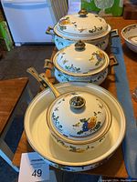 Full view of the 7-piece Villeroy & Boch metal cookware set with colorful floral patterns and brass handles, displayed on wooden table.