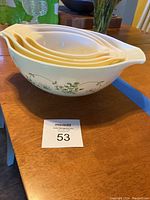 Stacked set of four pale yellow Pyrex mixing bowls with green floral vine pattern on the side. Bowls feature handles and pouring spouts, shown nested together.