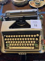 Vintage Olympia manual typewriter top front view showing keyboard and original case base, keys include letters, numbers, and function keys TAB, clear, set in green, cream body.