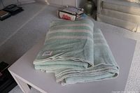 Two folded light green wool blankets with pale cream horizontal stripes displayed on a table.