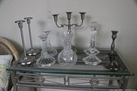 Full view of 11 assorted candle holders including pewter, glass, and metal pieces arranged on glass table.