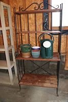 Full front view of black metal framed Backer's rack with four wooden shelves. Some gardening items placed on middle shelves.