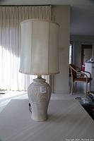 Beige ceramic table lamp with etched design, fitted with a large cream fabric shade.