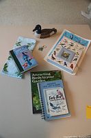 Photo showing entire birdwatchers' lot on a beige surface, including books, laminated bird posters, a carved wooden duck, a cloth, and a keychain.
