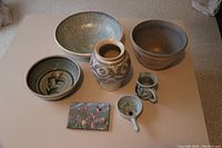 Overview of the pottery set and the enamel wall art on a white table.