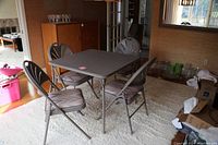 Bridge table and 4 folding chairs arranged on a cream carpet near a window showing overall lot setup.
