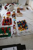 Wide view showing various children's toys including building blocks, toy clock, vehicle, and other assorted items on a white sheet.