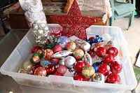 Plastic bin containing assorted Christmas ornaments including balls in multiple colors and styles with a large decorative red star on top.