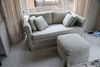Front view of small sage green couch with three seat cushions removed and matching ottoman in foreground