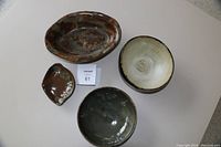 Top view of the pottery items on a white surface showing three bowls and one soap dish with varying green and brown glazes.