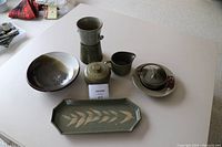 Overview of 7 green pottery pieces on a white table including bowls, covered jar, creamer, sugar bowl and tray.
