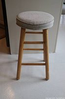 Side view of stool showing worn fabric seat and wooden legs with scuffs.